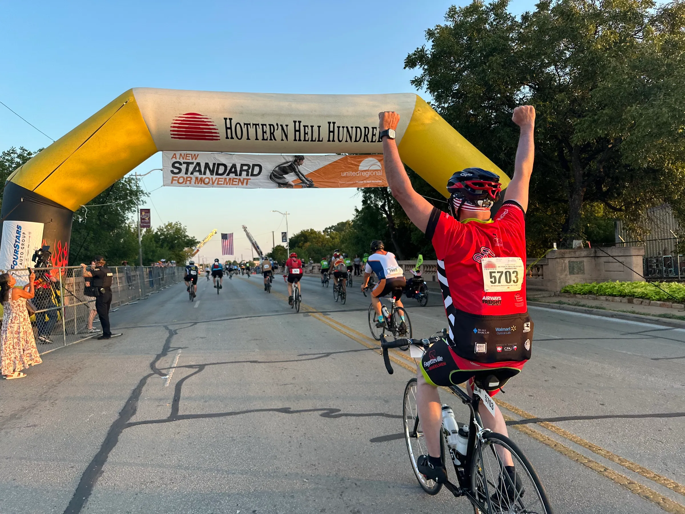 A cyclist raises both arms beneath the Hotter’N Hell Hundred finish arch.