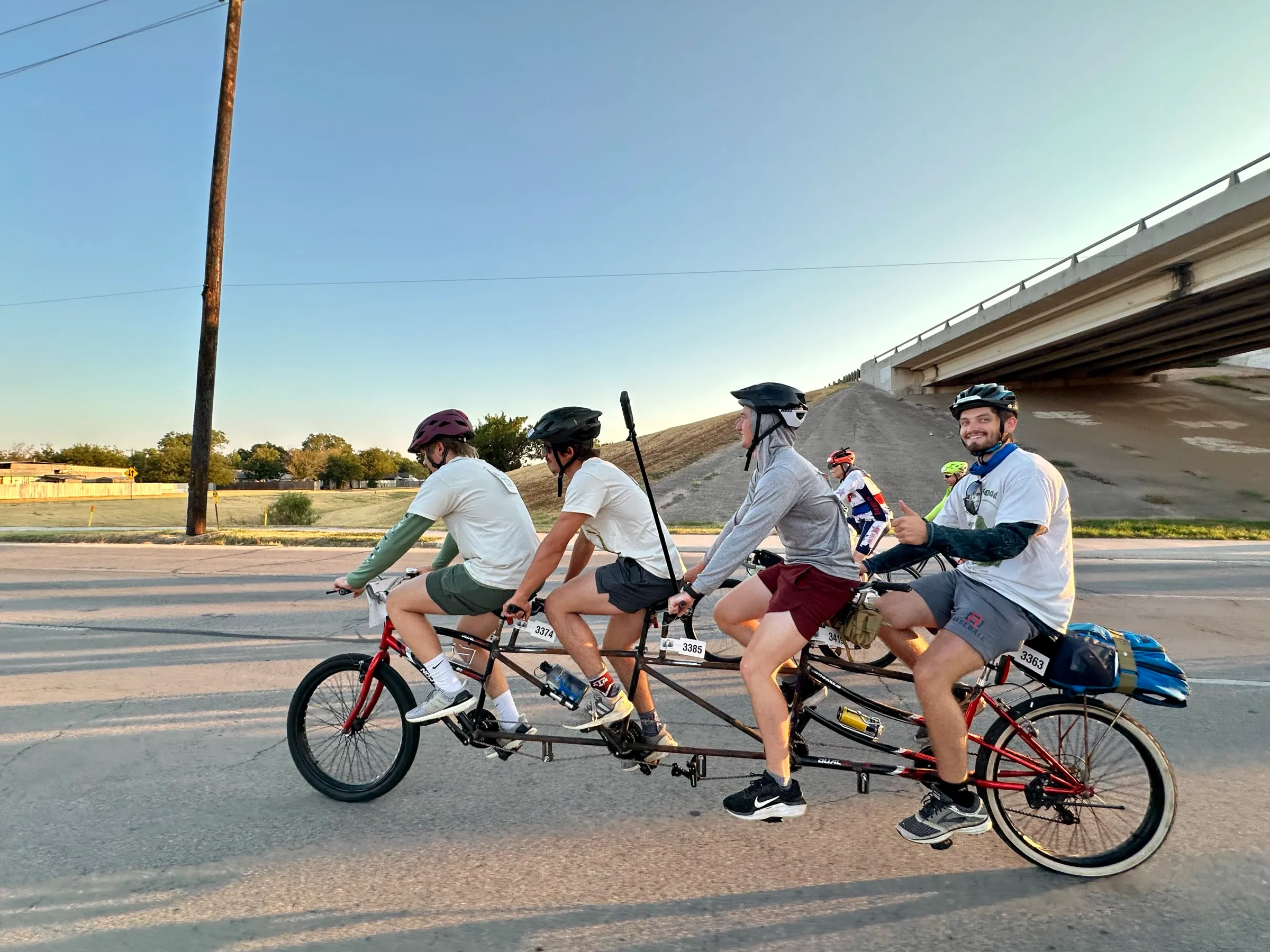 Riders on a multi-seat tandem bicycle travel alongside other cyclists on a Wichita Falls road.